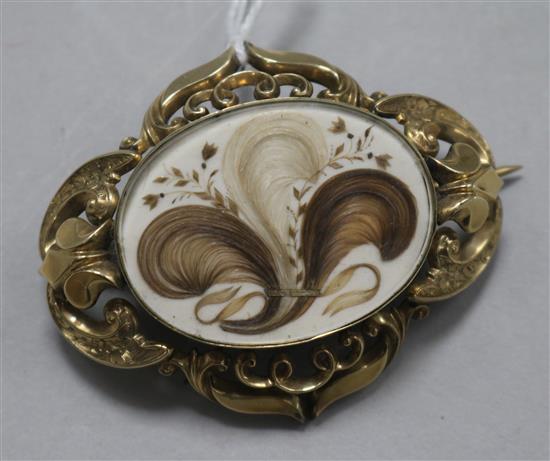 A Victorian pinchbeck brooch with central oval glazed hairwork panel in pierced and scrolled mount, 61mm.